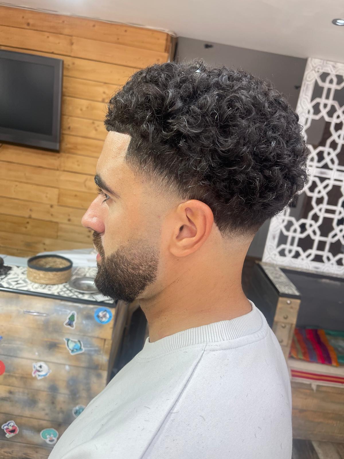 Curly top with a low taper fade and shaped beard